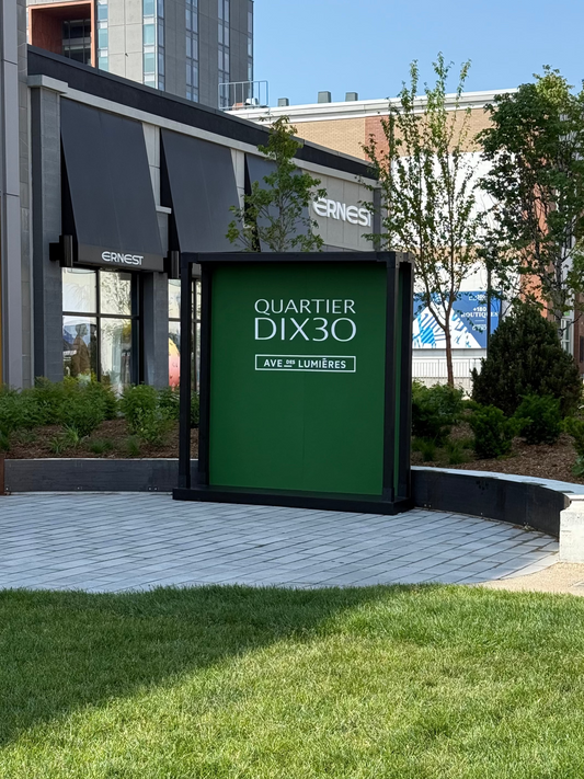 Green sign with 'Quartier Dix30' text in an urban setting