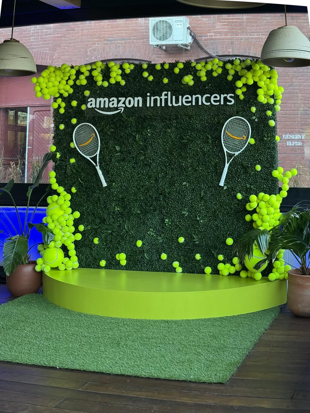 Decorative setup with 'Amazon Influencers' branding, tennis balls, and rackets on a green platform.