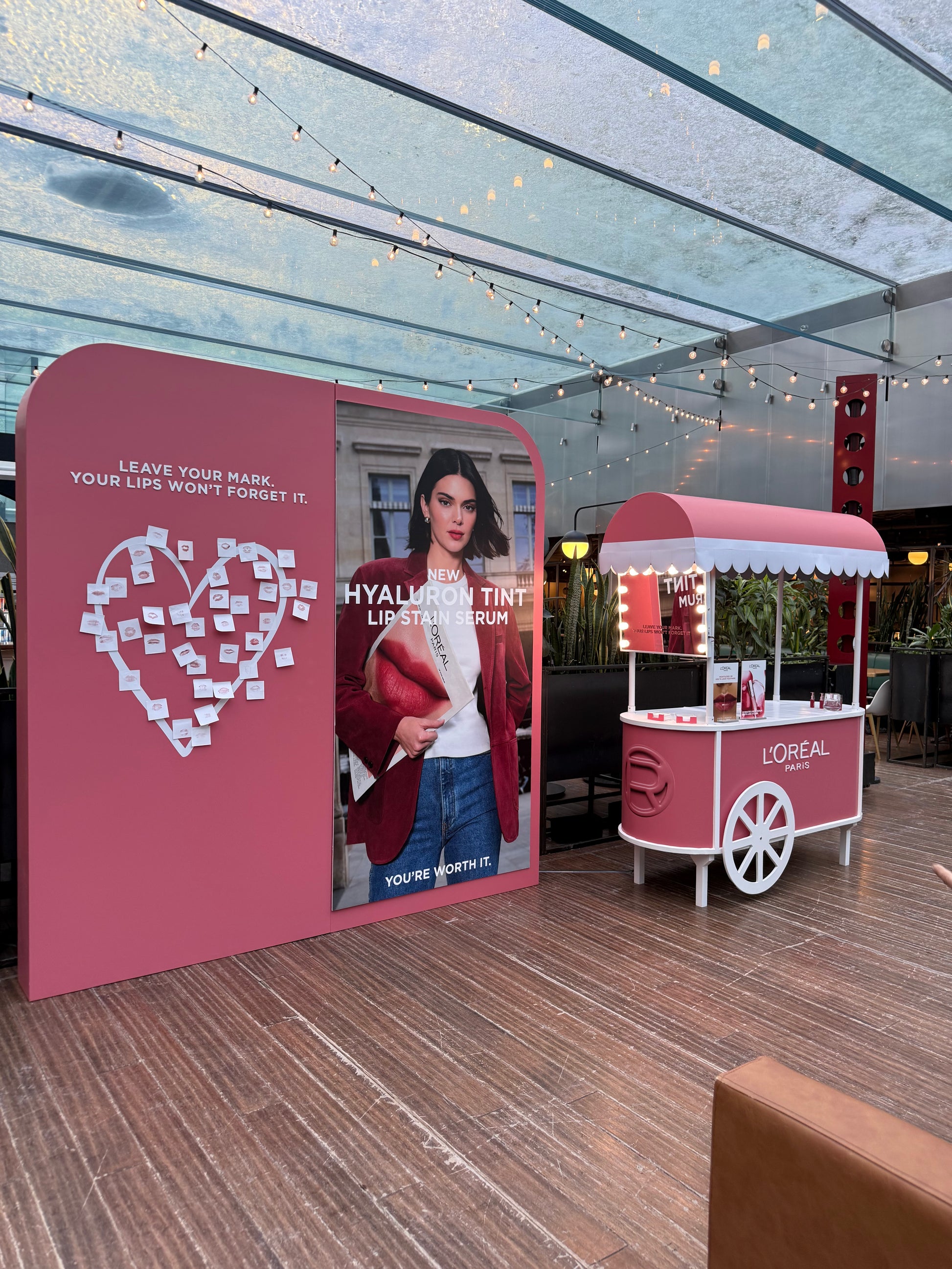 L'Oreal promotional stand with a display and a cart in an indoor setting.