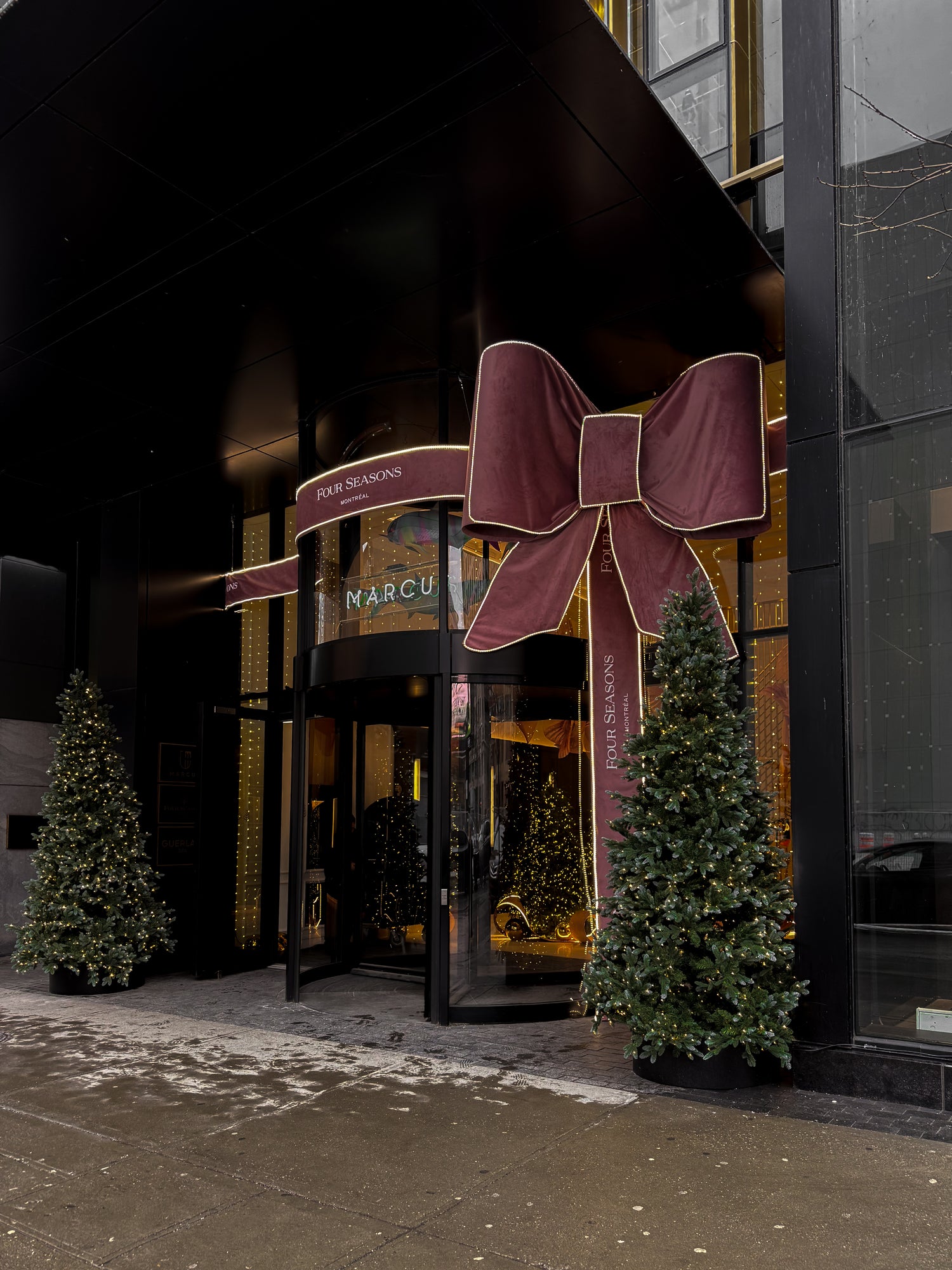 Luxurious storefront with a large decorative bow and 'Marcus' sign, surrounded by Christmas trees.